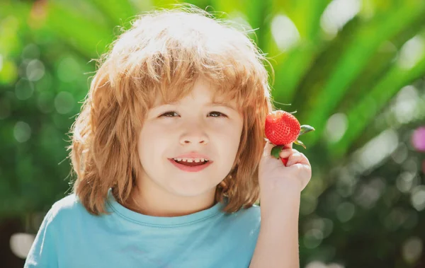 Kind mit glücklichem Gesicht beim Erdbeeressen. Kind hält Erdbeere in der Hand. — Stockfoto