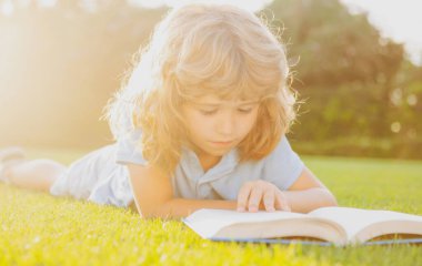 Çocuk kitap okuyor. Çocuk okulu ve açık hava eğitimi. Doğa ve park. Erken öğrenme. Açık havada yaz.