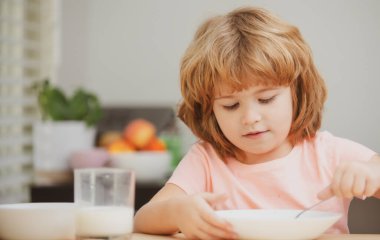 Bir tabak çorbası olan komik bir çocuk. Çocuk yemeği. Anaokulu çocuğu elinde kaşıkla sabah kahvaltısının tadını çıkarıyor..