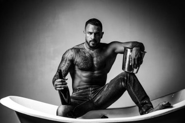 Şampanya kutlaması. Gri arka planda dövmeli yakışıklı bir adam. Seksi gece partisi, genç aşıklar. Kot pantolonlu moda adamı bacakları.