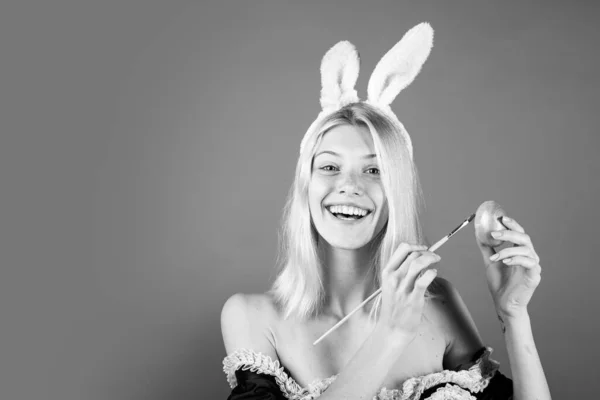 Vrolijke jonge vrouw die eieren schildert op een rode achtergrond. Schattig konijntje. Aantrekkelijke jonge vrouw met konijnenoren. Gelukkig Pasen. — Stockfoto