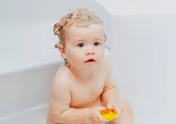 Vicces baba fürdik fürdőkádban vízzel és habbal. A gyerekek higiéniája. Kisgyerek a fürdőkádban. Mosolygós gyerek a fürdőszobában játék kacsa. — Stock Fotó