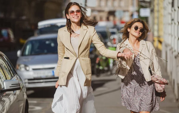 Ενθουσιασμένες ευτυχισμένες γυναίκες που περπατούν μαζί στο δρόμο. Ευτυχισμένες όμορφες γυναίκες φίλες με φόρεμα μόδας περπατώντας και τρέχοντας χαρούμενες και χαρούμενες χαμογελαστές στην πόλη. — Φωτογραφία Αρχείου