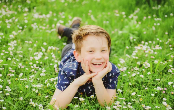 Leende pojke liggande på bekymmerslöst blomsterfält. Söt unge barn njuter på fältet och drömmer. — Stockfoto