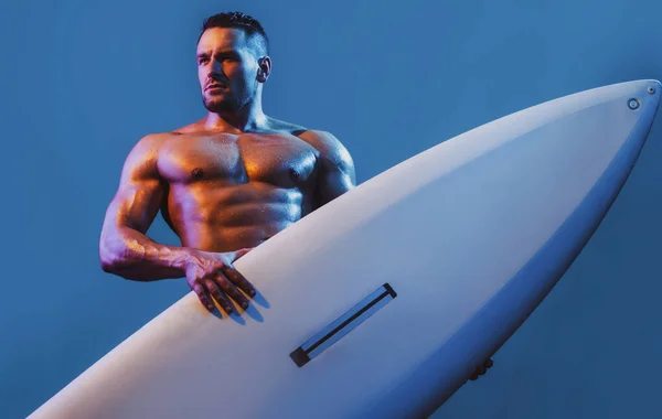 Een man op het strand met surfplank. Een jonge surfer met een lijfplank. Zomervakantie concept. Sexy gespierde surfer met een surfplank. Zomer jongen, geïsoleerd op blauw. — Stockfoto