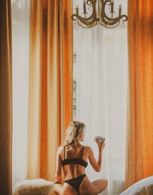 Yatak odasındaki genç ve sağlıklı kadınların arka görünüşü. Sabah kahve içerken. Evde yatağında kahve fincanları olan rahat, genç, şehvetli bir manken. Neşeli seksi sabah kızı.