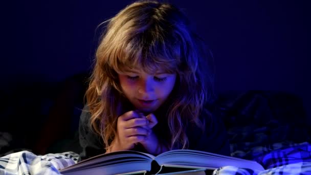 Ένα παιδί διαβάζει ένα μαγικό βιβλίο στο κρεβάτι. Ο μικρός διαβάζει βιβλία στο σπίτι.. — Αρχείο Βίντεο