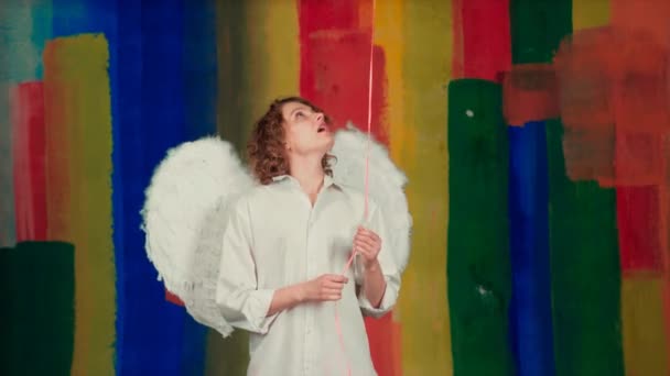 Angel γυναίκα με αερόστατο στέλνει ένα φιλί αέρα πάνω από πολύχρωμο φόντο. Νεαρή αγγελική γυναίκα με αστείο χαμογελαστό πρόσωπο και μπαλόνι καρδιάς. — Αρχείο Βίντεο