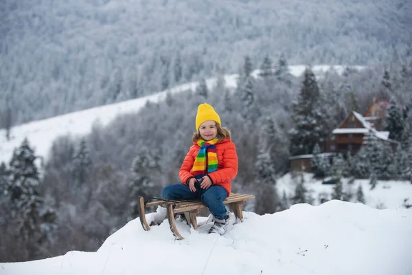 Örgü şapka, atkı ve süveter giyen mutlu küçük çocuğun portresi. Çocuk kızakla gezmekten zevk alıyor. Kış eğlenceli çocuk aktiviteleri. Kış örgü çocuk kıyafetleri.. — Stok fotoğraf