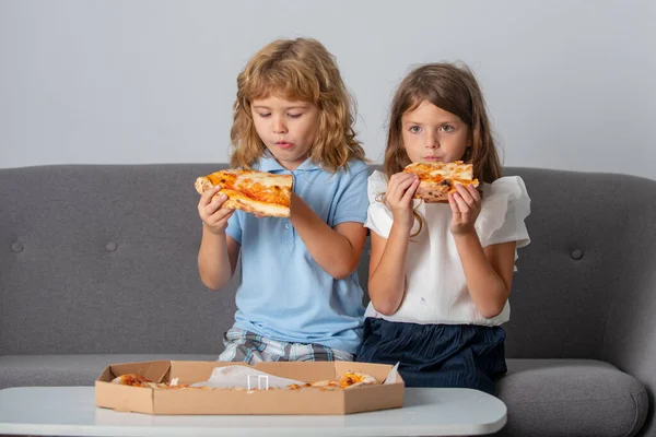 Niños hambrientos comiendo pizza. Niños pequeños amigos, chico y chica muerden pizza. Comida rápida poco saludable. — Foto de Stock