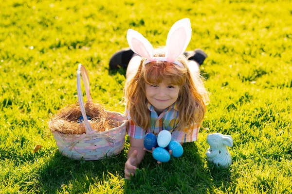 Kinderen die op paaseieren jagen. Kind in konijnenoren die paaseieren verzamelen, op gras leggen. Voorjaarsvakantie. — Stockfoto