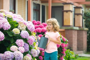 Bahçede sulama tenekesiyle çiçek sulayan şirin bir çocuk. Küçük sevimli bir çocuk ailesinin çiçek yetiştirmesine yardım ediyor. Çocuklarla aktif tatiller.