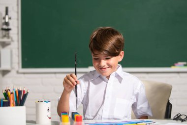 Resim ödevi yapan, elinde kalem tutan, yazı yazan okul çocuğu. Çocuk ilkokulda resim çiziyor. Çocukluk eğitimi, çocukların sanatsal becerileri..