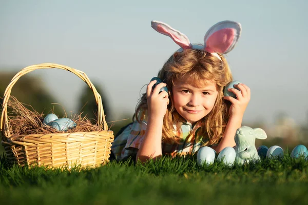 Niño con huevos de Pascua en cesta al aire libre. Niño acostado en la hierba en el parque en el fondo del cielo con espacio de copia. Caza de huevos de Pascua. Fynny cara de niños. —  Fotos de Stock