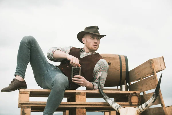 Cowboy kalapban. Vonzó férfi whiskyvel vagy brandyvel. Nyugati élet. Jóképű szakállas nyugati farmer. Férfi cowboy vagy farmer portréja. Nyugati. — Stock Fotó