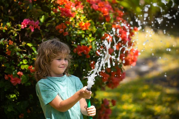 Щасливий хлопчик поливає воду зі шлангу. Дитинство американських дітей. Дитина поливає квіти в саду. Домашнє городництво. — стокове фото