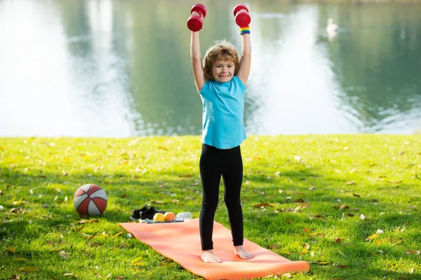Deporte infantil. Lindo niño haciendo ejercicios con pesas en el parque verde. Retrato de niño deportivo con mancuernas. Niño feliz haciendo ejercicio al aire libre. Actividades saludables estilo de vida de los niños. —  Fotos de Stock