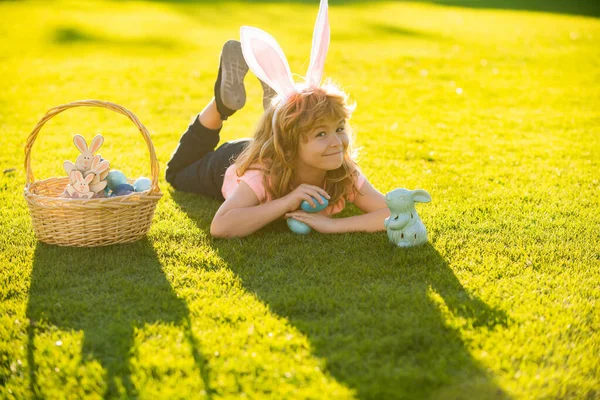 Vrolijk Pasen. Kind jongen met paaseieren en konijnenoren op gras. — Stockfoto