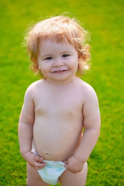 Porträtt av en liten pojke i blöja som leker utomhus i gräset. Baby och sommar soligt väder. Lustigt litet barnporträtt. Blond grabb, skrattande känslor, glad leende ansikte. — Stockfoto