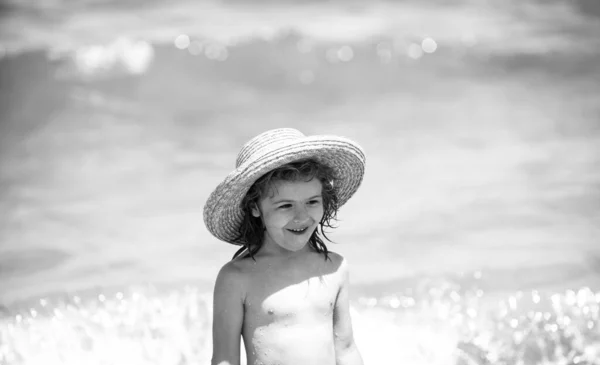 Liebenswerter kleiner Junge mit Strohhut am Strand während der Sommerferien. Porträt eines verspielten Kindes vor dem Hintergrund des Meeres. Lustiges Sommer-Kindergesicht. — Stockfoto