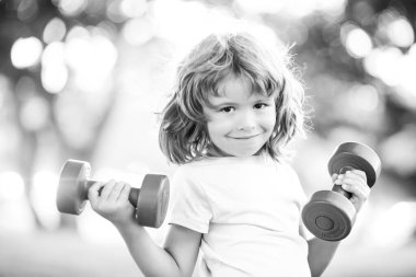 Çocuk halterleri egzersiz yapıyor. Dambılı açık havada sportif bir çocuk. Çocuklar spor yapar. Parkta çocuk antrenmanı. Çocuklar aktif, sağlıklı yaşam tarzı.