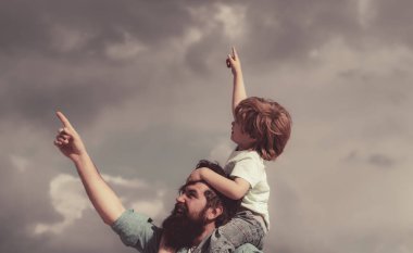 Babalar Günü. Babasıyla dışarıda oynayan sevimli çocuk. Mutlu çocuk yaz gökyüzünü işaret ediyor..