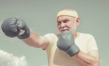 Boks pozisyonunda kıdemli sporcu boks eldivenleriyle egzersiz yapıyor. Aktif boş zaman. En iyi kardiyo çalışması.
