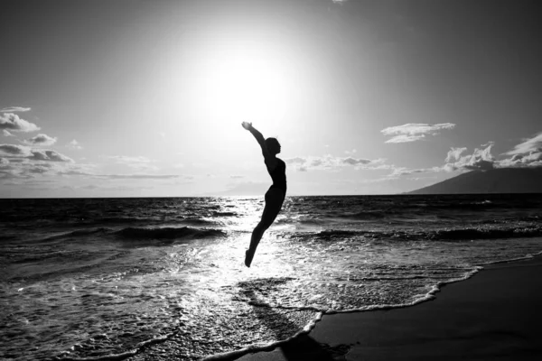 一个无忧无虑的女人，高举双手，在大海和蓝天的映衬下跳跃着。暑假、旅行和自由的概念. — 图库照片