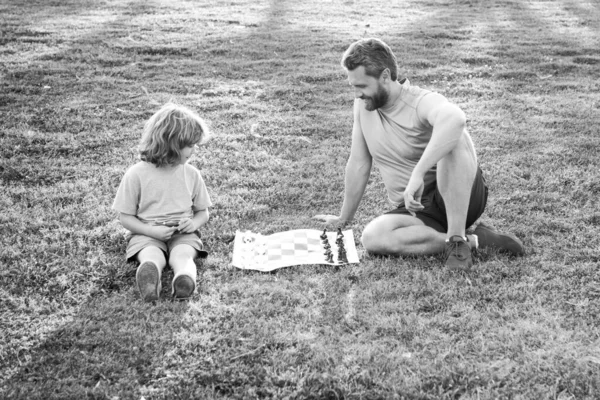 Отец и сын, маленький мальчик играет в шахматы, проводит время вместе на открытом воздухе в летнем парке. — стоковое фото
