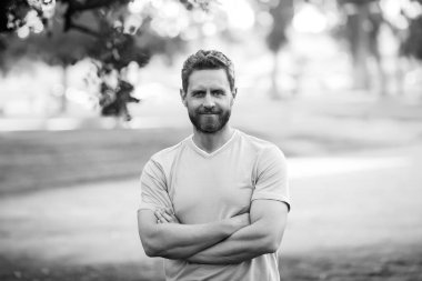 Parkta kollarını kavuşturmuş tişörtlü yakışıklı bir genç..