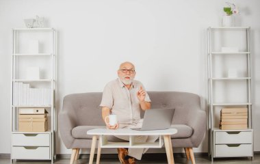 Yetişkin bir adam iş eğitimini izliyor, dizüstü bilgisayarda internetten giyiniyor, uzaktan kumandayla çalışıyor. Video konferansında yaşlı işadamı sanal sohbet çağrısı yapıyor.