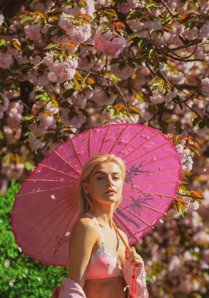 Spring girls in flowers. Japanese blossom. Beautiful young woman stands among flowering trees. Pink flowers. Spring portrait, romance. — Stock Photo, Image