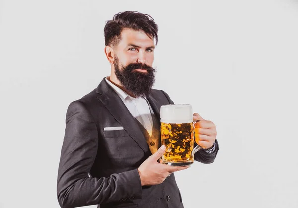 Ernsthafter Mann im klassischen Anzug trinkt Bier. Der bärtige Typ im Business-Outfit sieht glücklich und zufrieden aus. Porträt eines Mannes mit erhobenem hohen Glas Bier auf weißem Grund. — Stockfoto