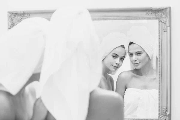 Fechar mulher bonita olhar no espelho após o chuveiro. Jovens amigas meninas bonitas envolto em toalha alisamento aperfeiçoando a pele, conceito de rotina da manhã diária. — Fotografia de Stock