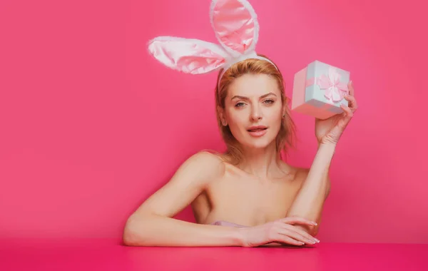 Retrato de una feliz niña de Pascua sosteniendo caja presente aislado sobre fondo rosa. Mujer joven con orejas de conejo. —  Fotos de Stock