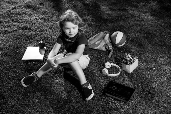 Kind mit Tablet-Gerät und Schulbedarf sitzt draußen im Garten, trägt Shorts und Hemd. Lttle Kind Outdoor-Schule, Bildung, Online-Fernunterricht. — Stockfoto