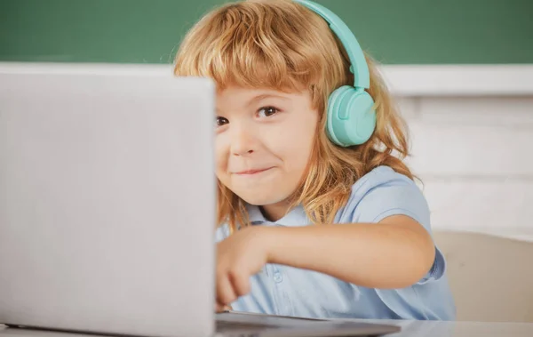 Primer plano retrato de niño lindo en auriculares usando un ordenador portátil y estudiar en línea con el profesor de videollamada en la escuela. — Foto de Stock