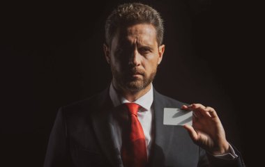 Kredi kartı olan kendine güvenen bir iş adamı. Formalite giyimli orta yaşlı bir iş adamı siyah giysiden izole edilmiş..