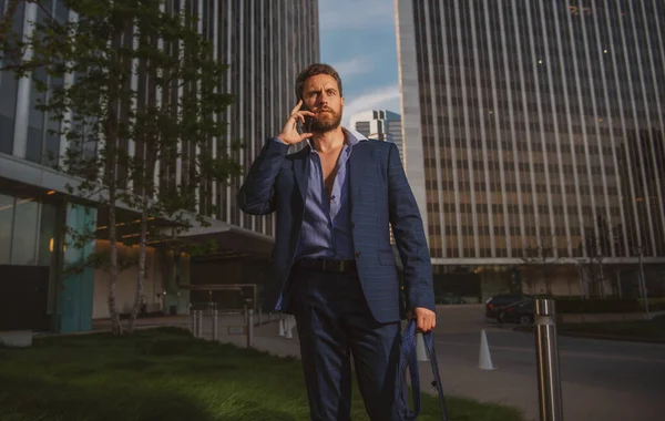 Retrato sexy homem de negócios usando smartphone perto de edifício moderno ao ar livre. Empresário bem sucedido andando de terno na rua. — Fotografia de Stock