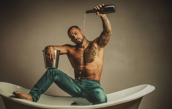 Sexy hombre desvestirse sentarse en la bañera en el baño, los hombres de vacaciones con champán. Celebrando Navidad o cumpleaños. Fiesta de sexo privado. — Foto de Stock