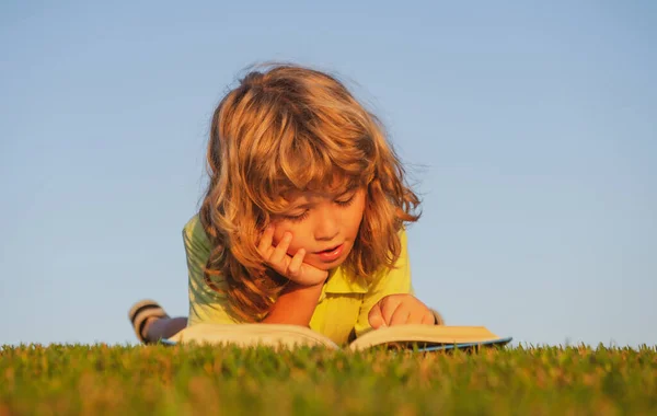 Libro inteligente de lectura infantil, tendido sobre hierba en el campo sobre el fondo del cielo. Retrato de niños inteligentes al aire libre. —  Fotos de Stock