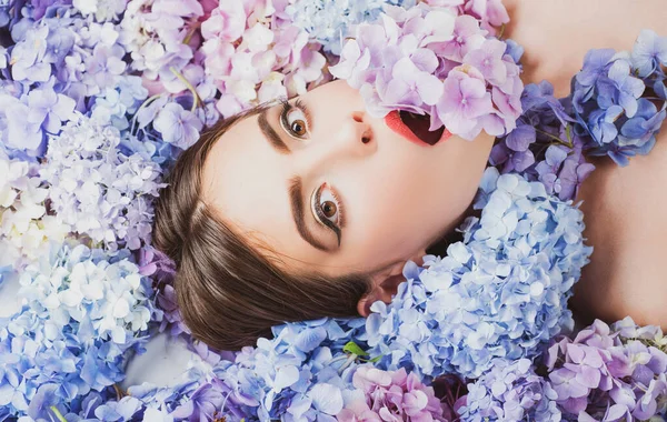Natuurschoon. Een vrouw die op bloemen ligt. Eenheid met de natuur. Blossom. Make-up cosmetica en huidverzorging. Meisje met hortensia bloemen. — Stockfoto