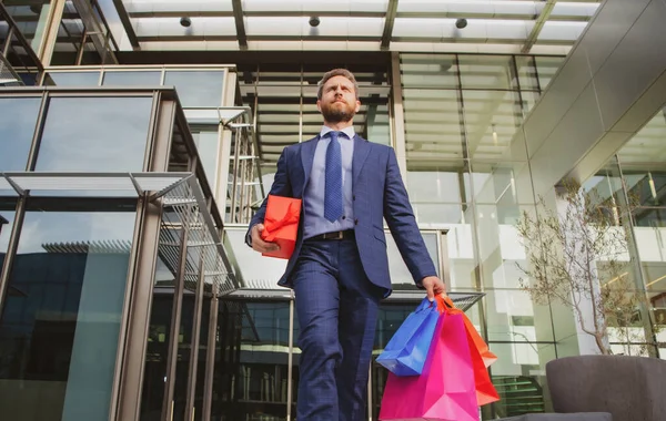 Όμορφος άντρας κάνει ψώνια στην πόλη. Πορτρέτο του επιχειρηματία στο κοστούμι με τσάντες ψώνια. — Φωτογραφία Αρχείου