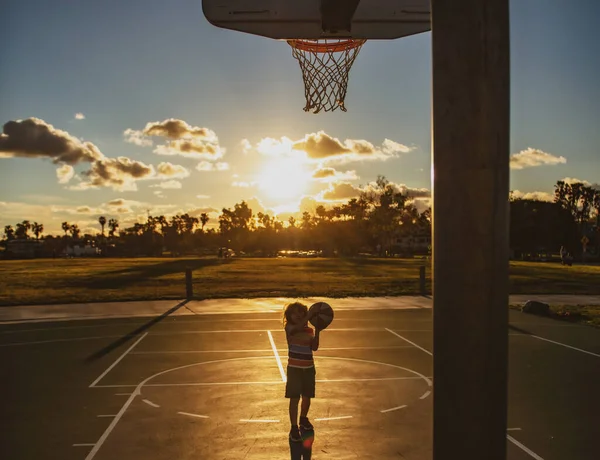 Chłopiec koncentruje się na grze w koszykówkę sylwetka na zachód słońca. — Zdjęcie stockowe