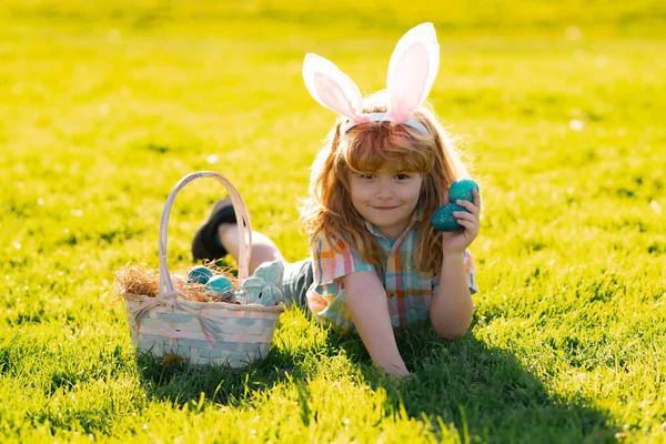 Kids jongen in konijnenoren jagen op paaseieren buiten. Kind met Pasen in het park. Paaseieren zoeken. Voorjaarsvakantie. — Stockfoto