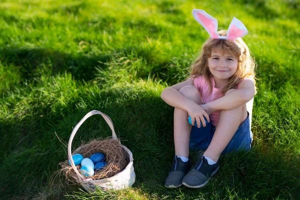 Słodkie dziecko z koszykiem wielkanocnym na trawie. Dziecko polujące na wielkanocne jaja. Cute kid w stroju królika z króliczymi uszami o Wielkanoc. — Zdjęcie stockowe