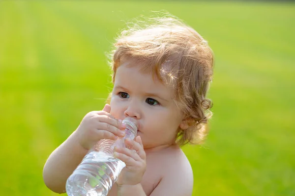 Bebé bebiendo agua. Beber agua de la botella al aire libre en el fondo de hierba. —  Fotos de Stock