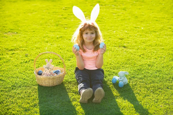 Kind met paaseieren en konijnenoren op gras. Gelukkige Pasen kinderen gezicht. Kinderen in konijnenoren op paaseieren jacht in de tuin. — Stockfoto