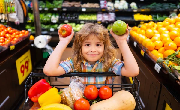 Der Junge kauft in einem Supermarkt ein. Kind wählt einen Apfel im Laden. Kleiner Junge wählt Apfel beim Einkauf im Obst- und Gemüsemarkt. — Stockfoto