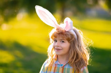 Tavşan çocuk suratı. Paskalya yumurtası avlayan çocuk. Tavşan kulaklı şirin çocuk parkta paskalya geçiriyor..